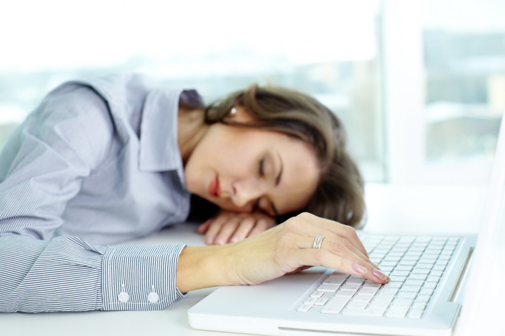 Young woman sleeping at workplace, her fingers touching keyboard